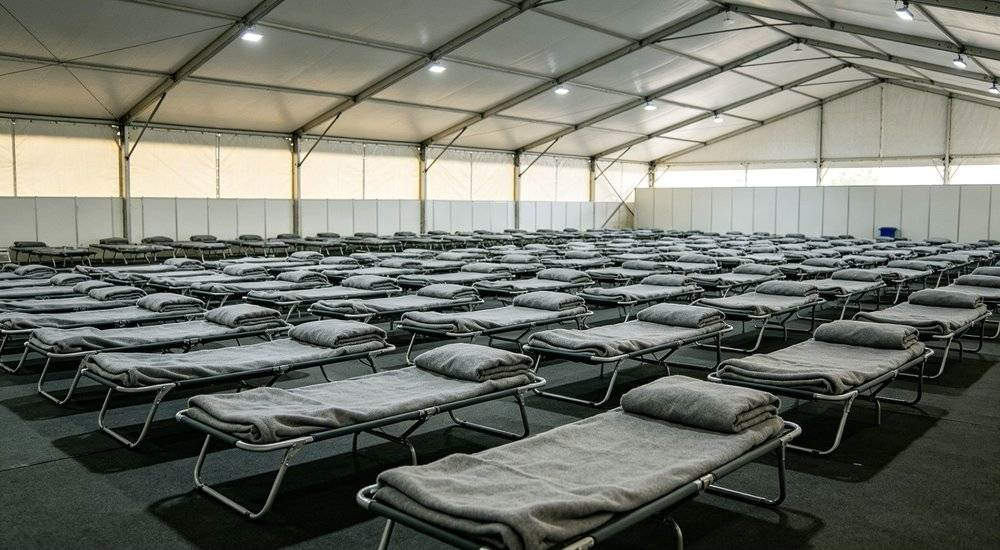 Eye-level interior of large event temporary worker housing with grey bedding on rows of beds for festival conference and sports event staff accommodation Eye-level interior of large event temporary worker housing with grey bedding on rows of beds for festival conference and sports event staff accommodation