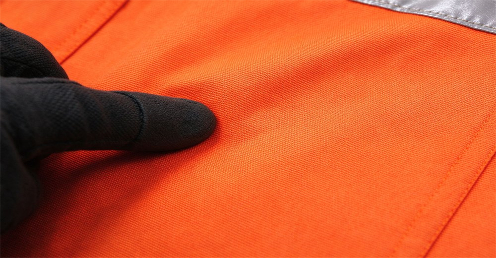 Gloved finger touches woven orange rescue suit fabric to show texture weave structure and stitching details Gloved finger touches woven orange rescue suit fabric to show texture weave structure and stitching details